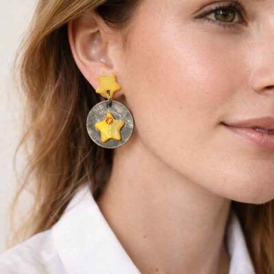 Pendientes artesanales de estrellas amarillas puestos en modelo con camisa blanca