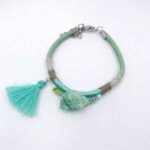 Pulsera verde con borla turquesa y detalles metálicos sobre fondo blanco