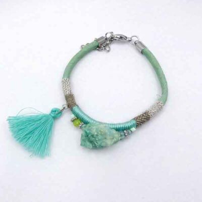 Pulsera verde con borla turquesa y detalles metálicos sobre fondo blanco