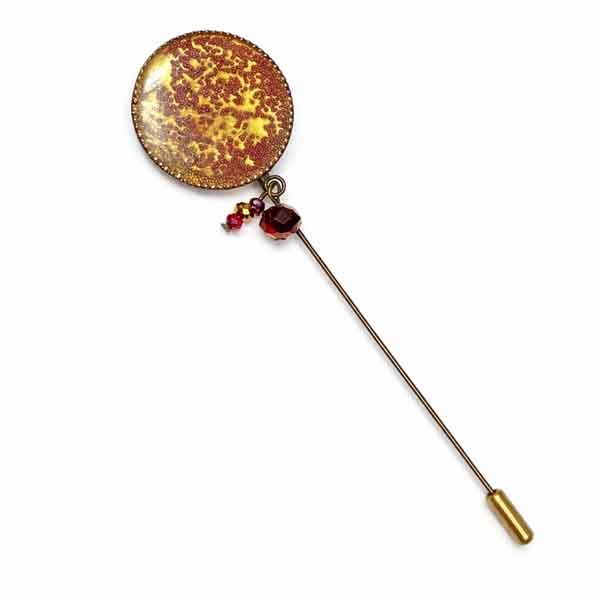 Aguja Planet artesanal única con inspiración planetaria Aguja Planet artesanal con cabujón esmaltado en tonos ámbar y burdeos, pieza única hecha a mano