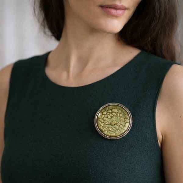 Broche artesanal único Camafeo Tierra sobre vestido verde oscuro de corte sencillo
