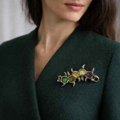 Broche artesanal Amaro hecho a mano con esmaltes en tonos verde, amarillo, ámbar y morado colocado sobre chaqueta verde oscuro