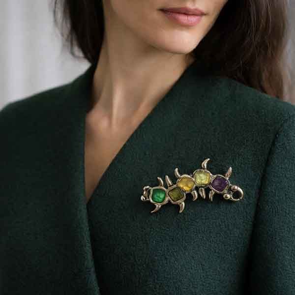 Broche artesanal Amaro hecho a mano con esmaltes en tonos verde, amarillo, ámbar y morado colocado sobre chaqueta verde oscuro