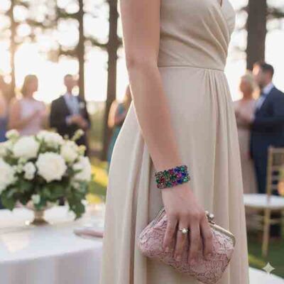 Modelo con vestido beige luciendo el brazalete Arcoíris, diseño elástico con piedras multicolor sobre base oscura, ideal para eventos elegantes.