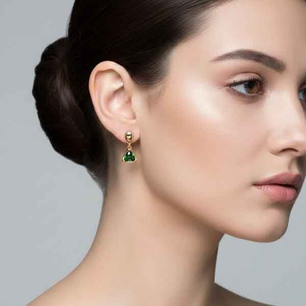 Modelo luciendo los pendientes Estigia triangulares en cristal verde con chapado en oro.
