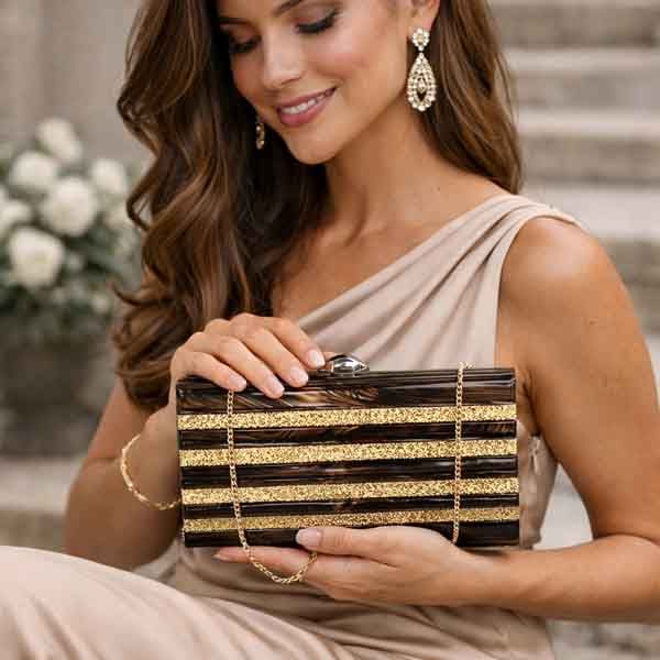 Bolso de fiesta marrón y dorado Berta en manos de modelo con vestido beige elegante