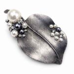 Broche de hoja en plata vieja con perlas en tonos gris y blanco sobre fondo claro