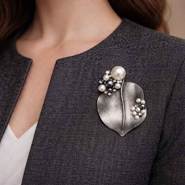 Broche de hoja en plata vieja con perlas en tonos gris y blanco colocado sobre chaqueta sin solapa