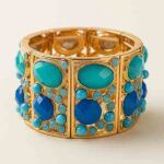 Brazalete Harmonía elástico con piezas símil piedra en tonos azul turquesa y azul klein sobre base dorada.