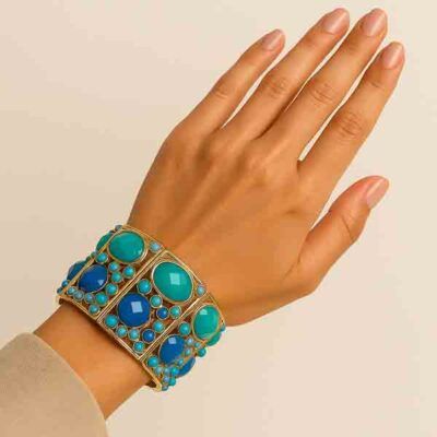 Mano femenina con el brazalete Harmonía elástico de piezas símil piedra en tonos turquesa y azul klein sobre base dorada.