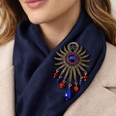 Broche Sol Kanpur en oro viejo colocado sobre foulard azul con abalorios rojos y azules