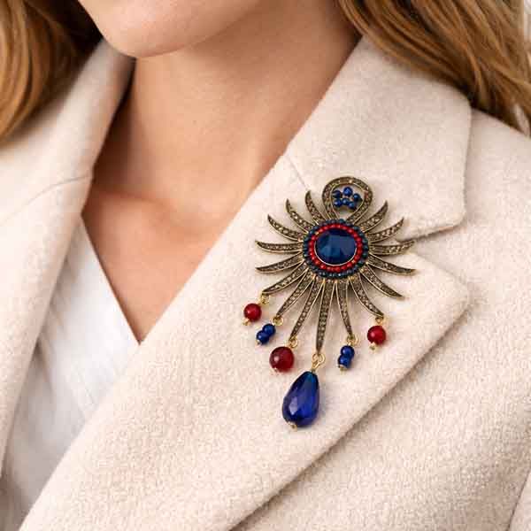 Broche Sol Kanpur en oro viejo colocado sobre chaqueta beige con piedra azul central