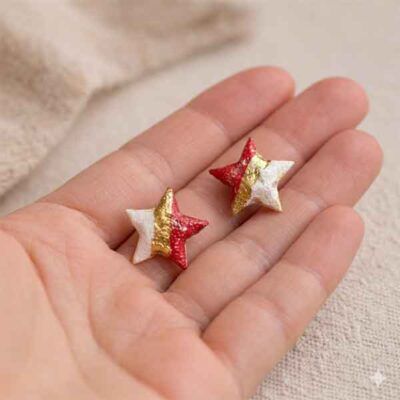 Pendientes de estrella de porcelana artesanales en blanco, granate y oro en la mano