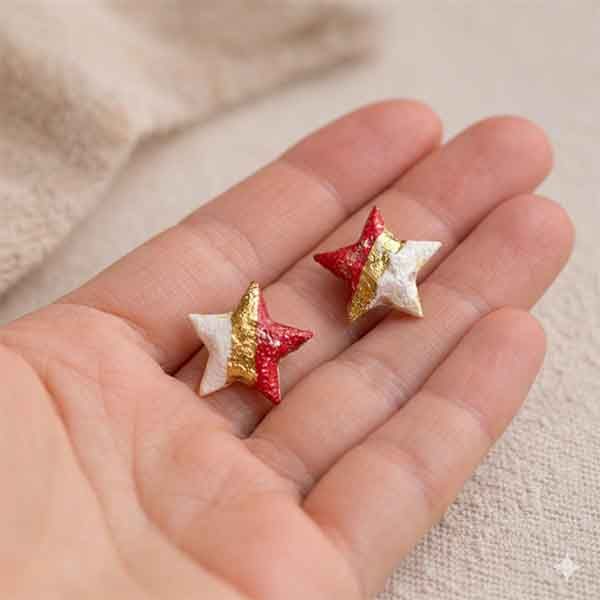 Pendientes de estrella de porcelana artesanales en blanco, granate y oro en la mano