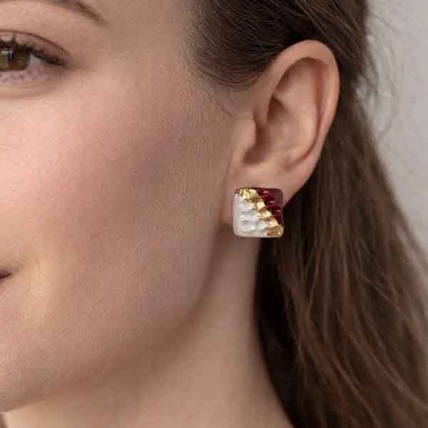 Pendientes Jolie de porcelana artesanales en forma cuadrada blanco nacarado, granate y oro puestos en la oreja