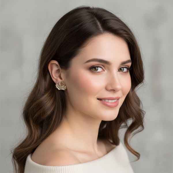 Pendientes de hoja dorados artesanales colocados en oreja de mujer, diseño inspirado en la naturaleza, ligeros y elegantes.