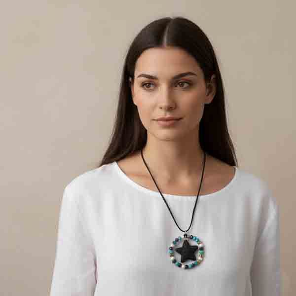Modelo con blusa blanca luciendo el collar Aurora artesanal, con cordón de ante negro y colgante circular con estrella de piedra negra y cuentas multicolor.