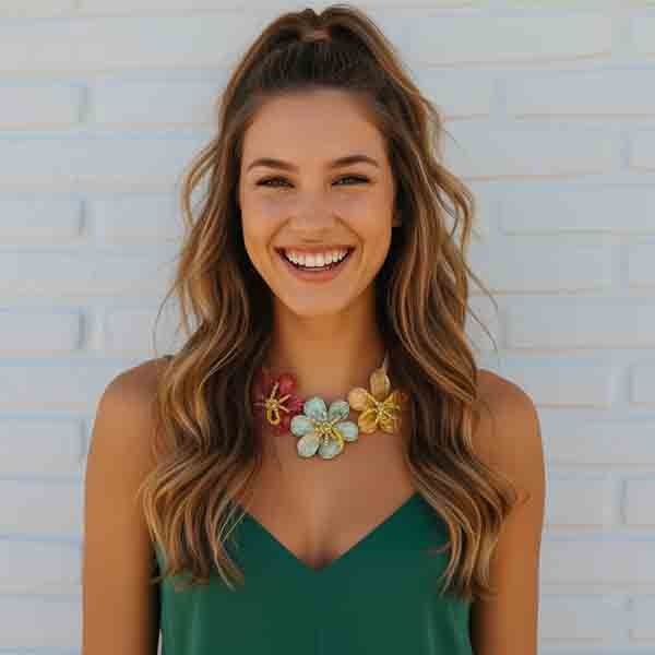 Modelo sonriente con look natural luciendo el collar Montsi, con tres flores de resina nacarada en tonos rojo, azul celeste y dorado, decoradas con cuentas de vidrio.