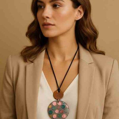 Mujer con el Collar Piruleta de resina, cordón negro y medallón con topos de colores, combinando con blusa blanca y americana beige.