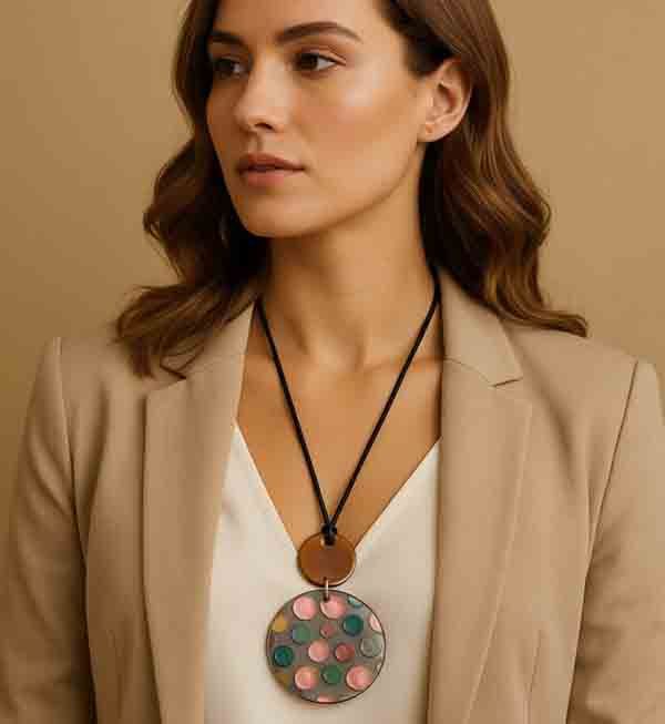Mujer con el Collar Piruleta de resina, cordón negro y medallón con topos de colores, combinando con blusa blanca y americana beige.