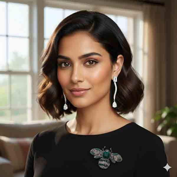 Mujer con vestido negro luciendo el Broche Hayar con cristales verde botella y gris ahumado en el escote, complementando un look elegante de interior.