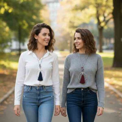 Dos modelos luciendo el collar Greta, uno con borla azul marino y otro con borla burdeos, diseño largo con aro plateado y cordón gris, bisutería artesanal moderna para mujer.