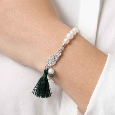 Pulsera de perlas con ala y borla verde puesta en la muñeca de una modelo