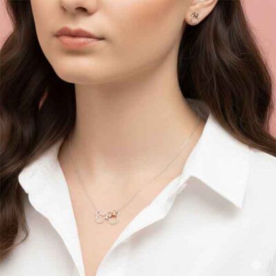 Collar de plata con siluetas Mickey y Minnie y lazo rosa llevado por mujer con camisa blanca