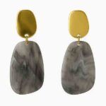Pendientes Nebbia con cabezal de acero dorado y colgante de resina marmolada gris sobre fondo blanco.