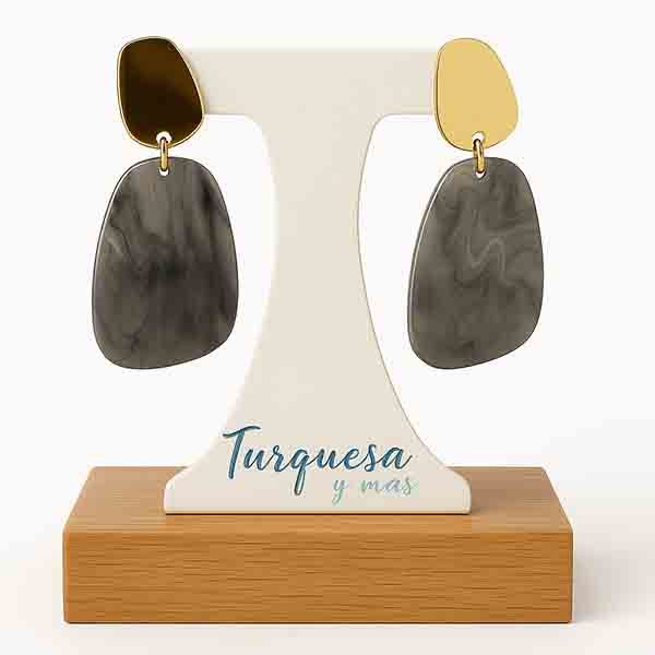 Pendientes Nebbia sobre base de madera clara, con cabezal de acero dorado y colgante en resina marmolada gris.