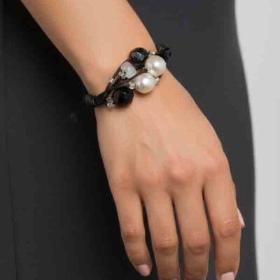 Pulsera Atenea negra con perlas y cuentas negras sobre cordón trenzado, lucida por una modelo con vestido negro.