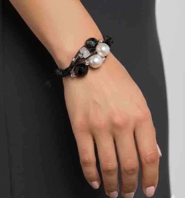 Pulsera Atenea negra con perlas y cuentas negras sobre cordón trenzado, lucida por una modelo con vestido negro.