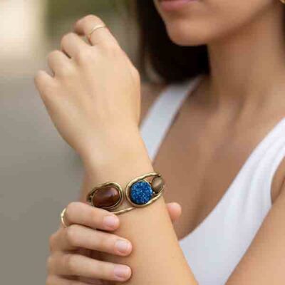 Mujer con la Pulsera Thalassa en metal dorado envejecido con piedras naturales en azul y marrón, combinada con look elegante y top blanco.
