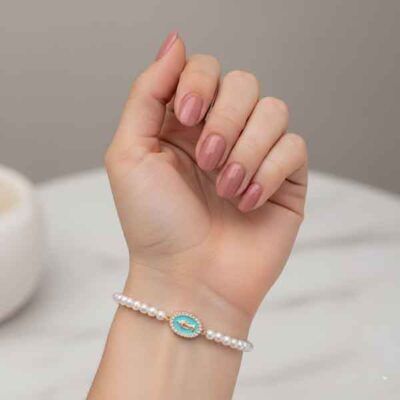 Pulsera de perlas con medalla Milagrosa dorada esmaltada en verde agua en la muñeca de una modelo