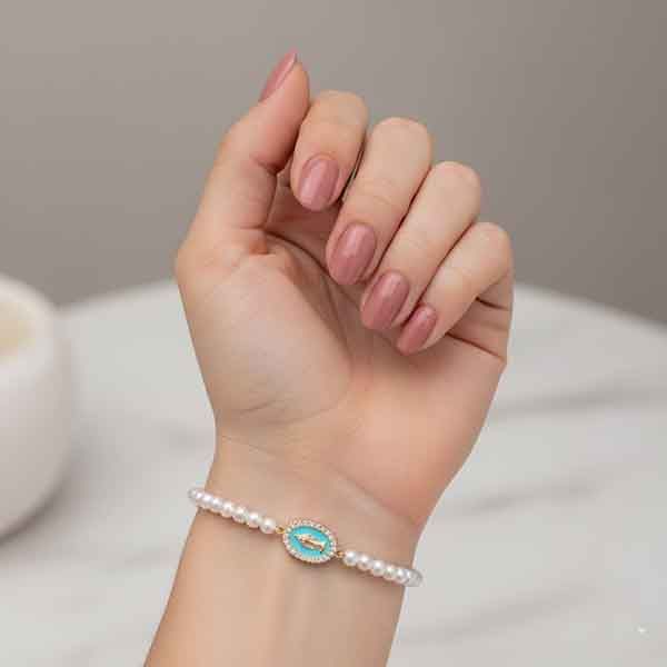 Pulsera de perlas con medalla Milagrosa dorada esmaltada en verde agua en la muñeca de una modelo