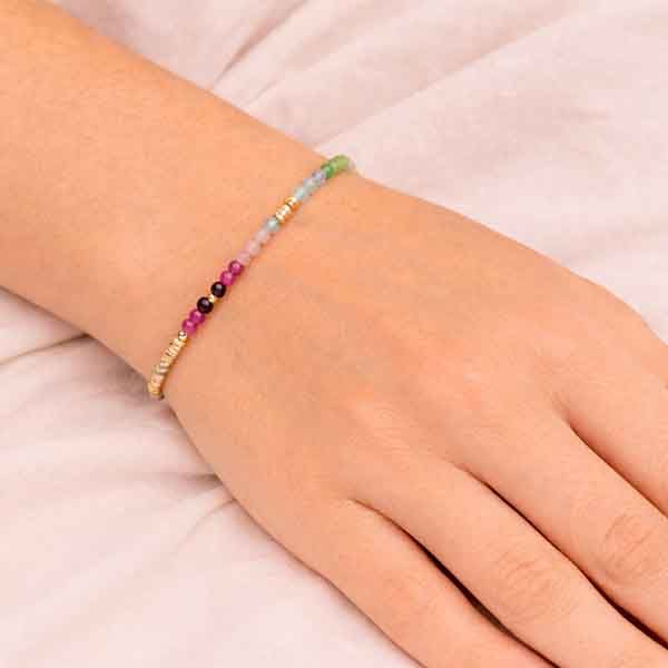 Pulsera de piedras multicolor con detalles dorados colocada en la mano de una modelo sobre fondo claro
