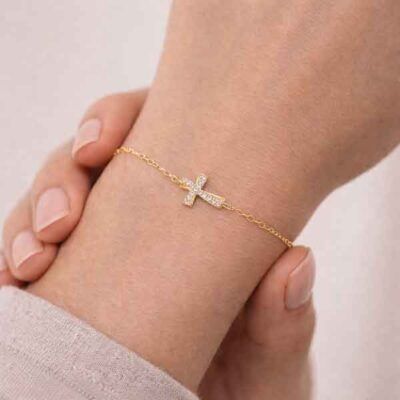 Pulsera de cruz ondulada bañada en oro con circonitas blancas en mano de modelo