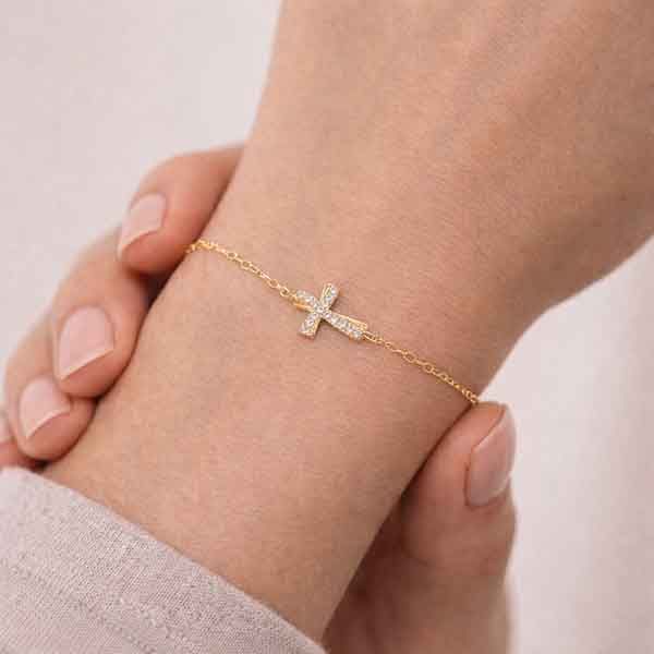 Pulsera de cruz ondulada bañada en oro con circonitas blancas en mano de modelo