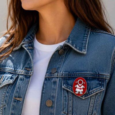 Broche Pamplonica pintado a mano colocado en el bolsillo de una cazadora vaquera. Diseño exclusivo de Turquesa y Más inspirado en San Fermín, Pamplona y la colección Rojo y Blanco de Colores de mi Tierra.