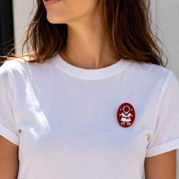 Broche Pamplonica pintado a mano colocado sobre una camiseta blanca. Diseño exclusivo de Turquesa y Más inspirado en San Fermín, Pamplona y la colección Rojo y Blanco de Colores de mi Tierra.